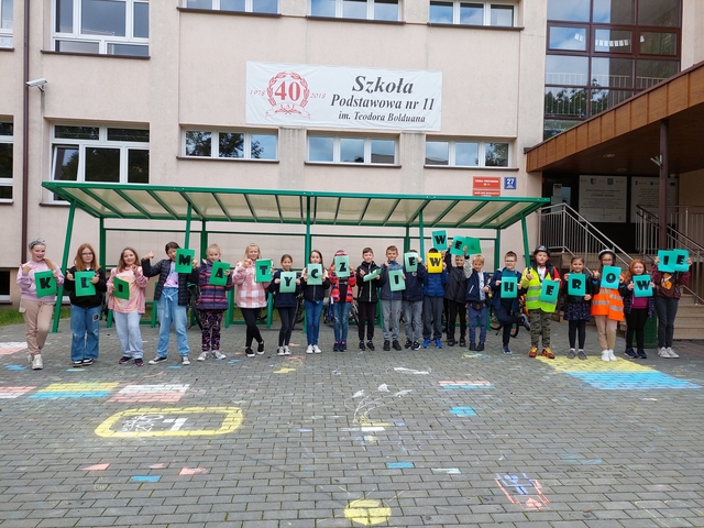 Uczestnicy akcji klimatycznie w Wejherowie trzymający napis "Klimatycznie w Wejherowie" na tle Szkoły Podstawowej nr 11