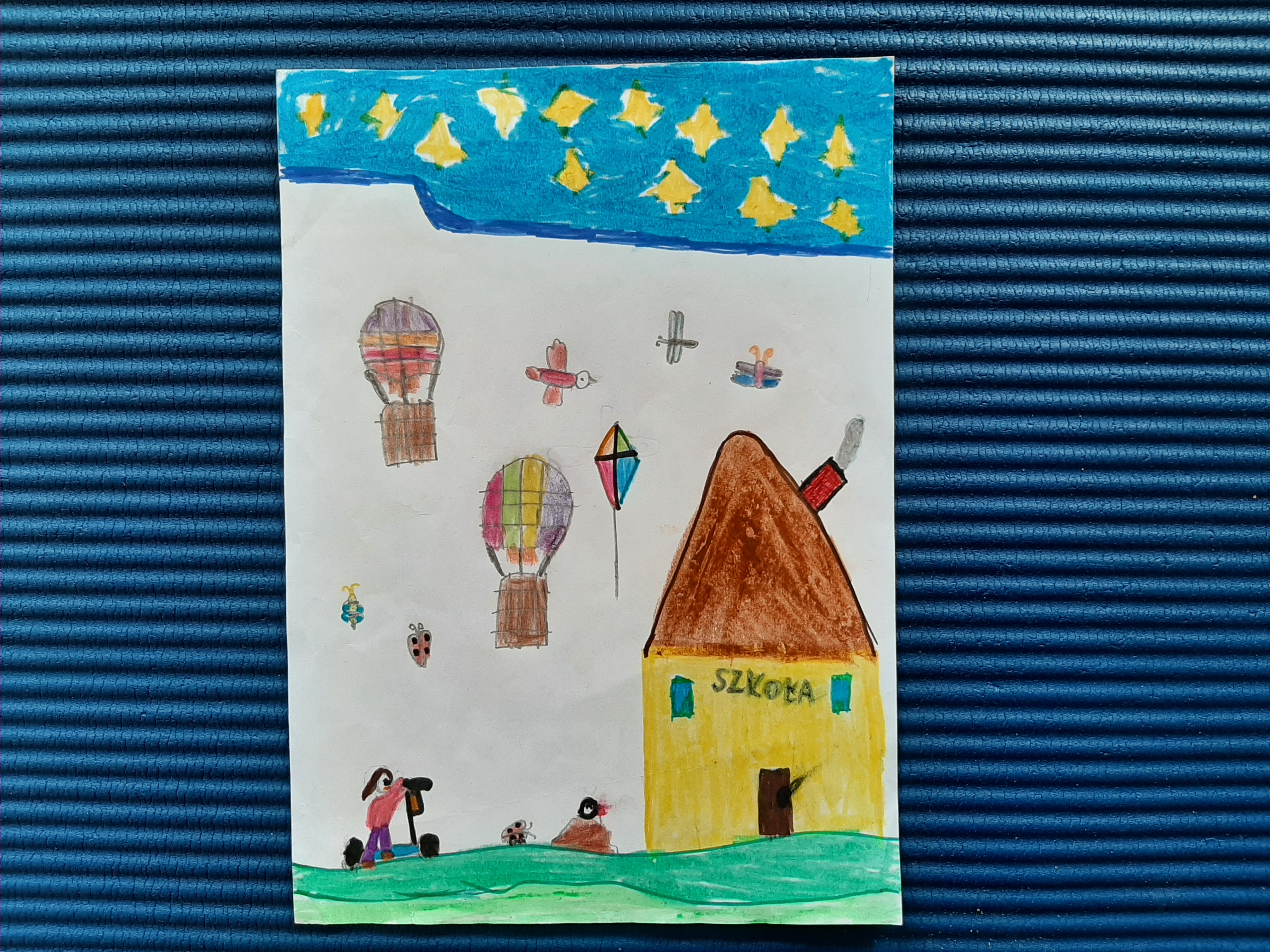 Na rysunku jest dziecko jadące w kierunku budynku szkoły, w tle motyle, latawiec, balon