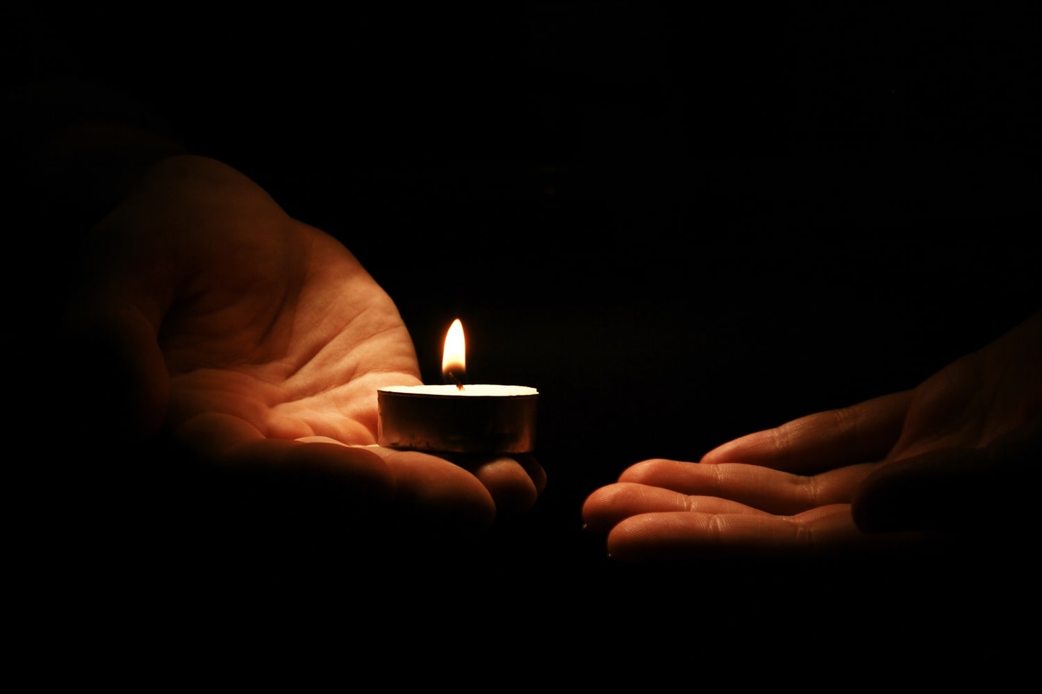 Mała świeczka trzymana w dłoniach na tle ciemnego tła