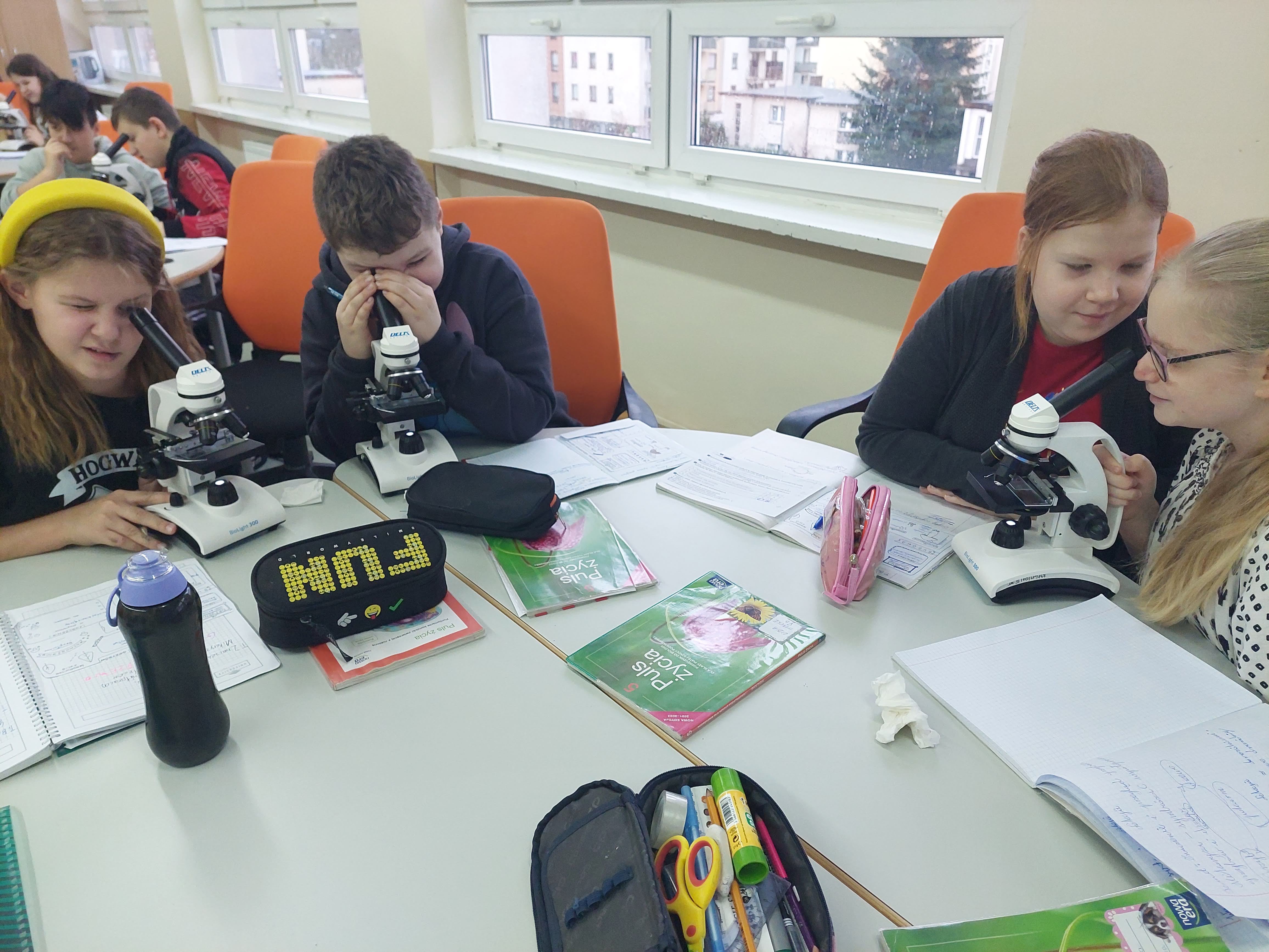 Uczniowie oglądający przez okular mikroskopu próbki