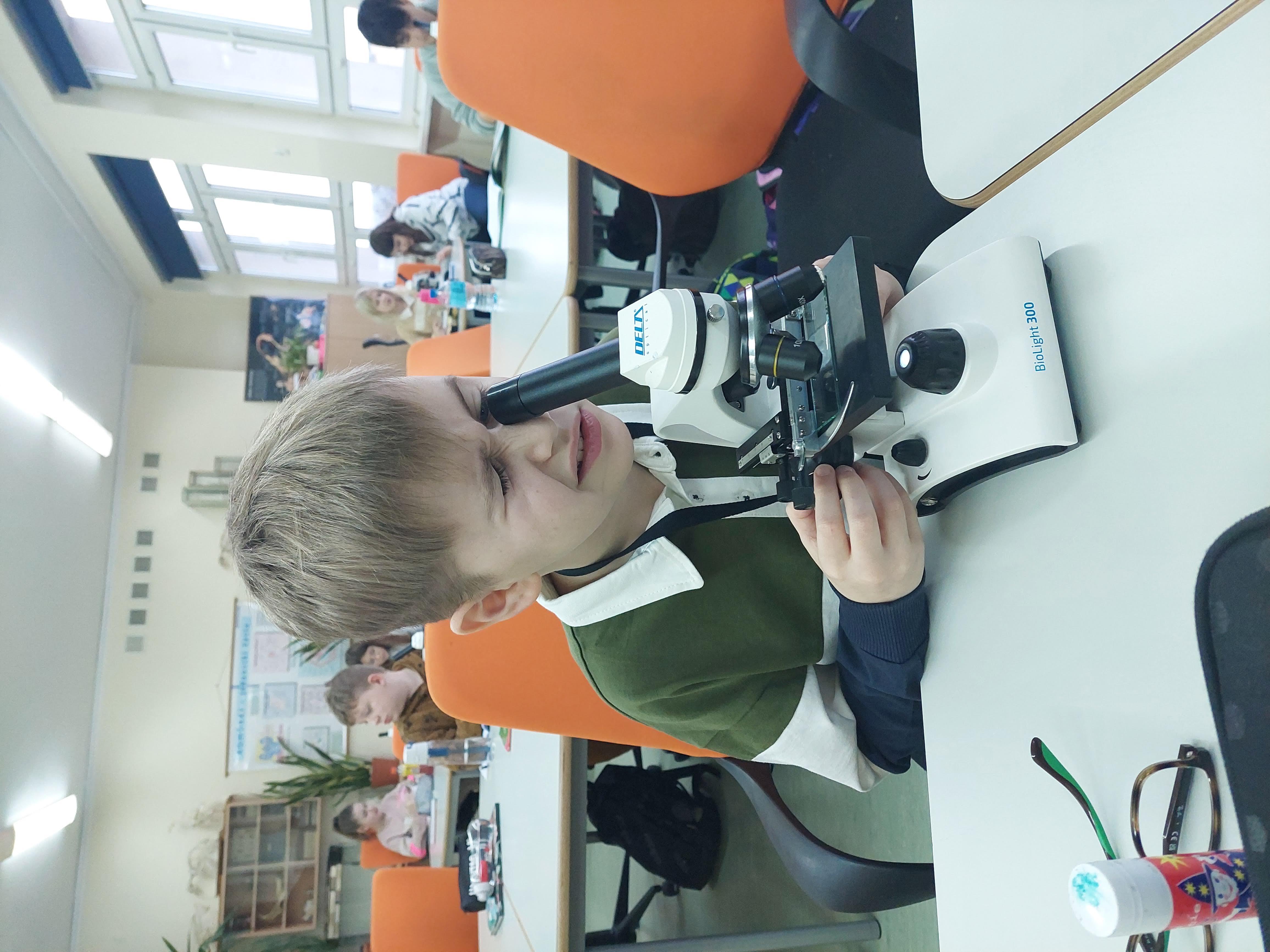Uczeń patrzący w okular mikroskopu w czasie lekcji. 