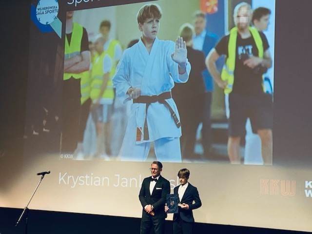 Chłopiec stoi na scenie, w ręku trzyma nagrody. Obok radny miasta Wejherowa. W tle prezentacja multimedialna, na niej wizerunek tego samego chłopca w stroju do karate.