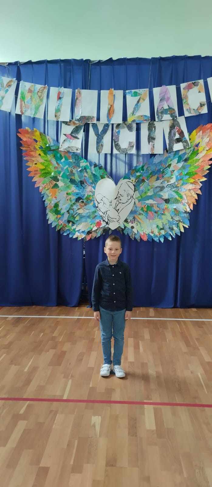 Na pierwszym planie widzimy chłopca – Nikodema, który stoi na tle niebieskiej dekoracji, na której są skrzydła z napisem „Cywilizacja Życia”. Na środku umieszczone jest zdjęcie Jana Pawła II z dzieckiem.
